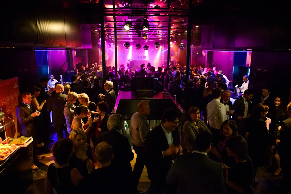 Bedrijfsfeest in een club met gasten in formele kleding, DJ en kleurrijke verlichting.