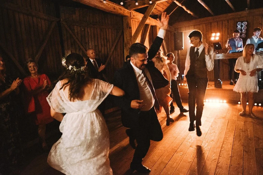 Gasten dansen uitbundig op de dansvloer tijdens een bruiloftsfeest met een DJ op de achtergrond in een houten schuur